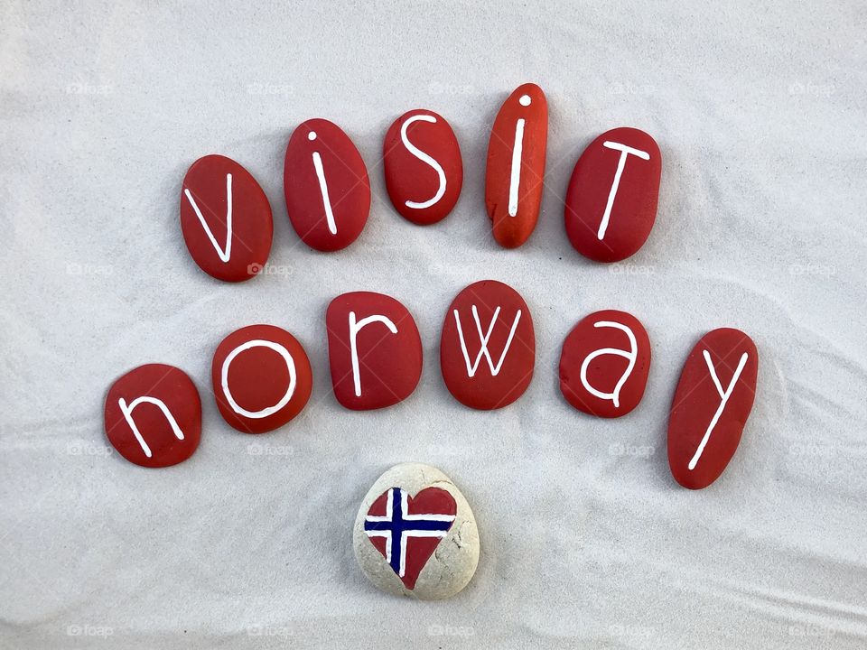 Visit Norway, creative composition with red colored stones and national flag over white sand
