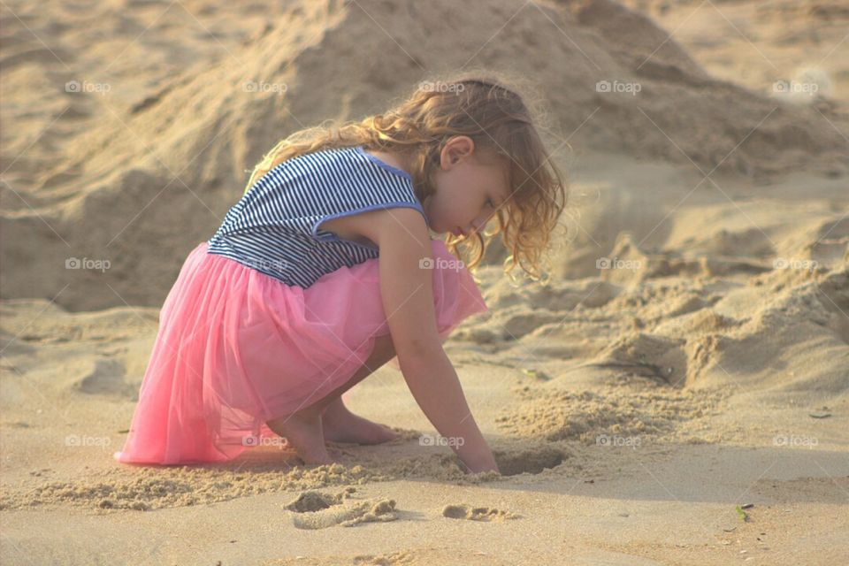 Pretty little girl digging in the sand at the beach. 