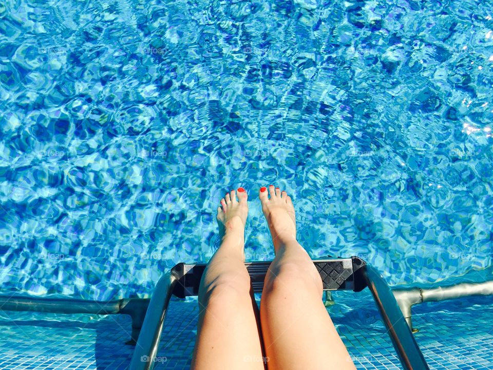 Woman's legs with red nail polish on the pool side