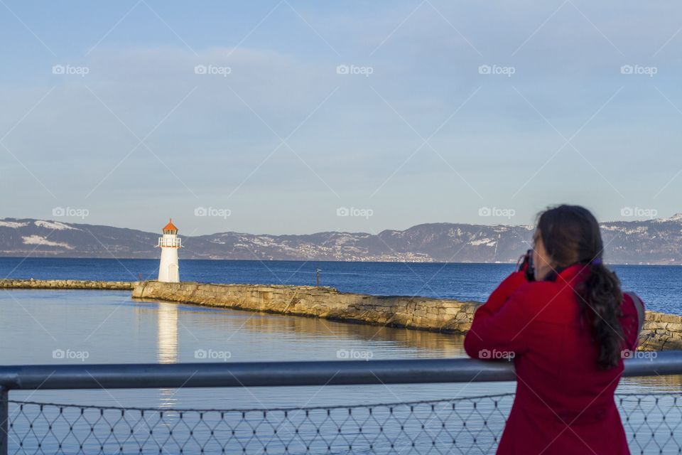 Girl and the lighthouse. A girl takes a picture of a lighthouse in Norway 