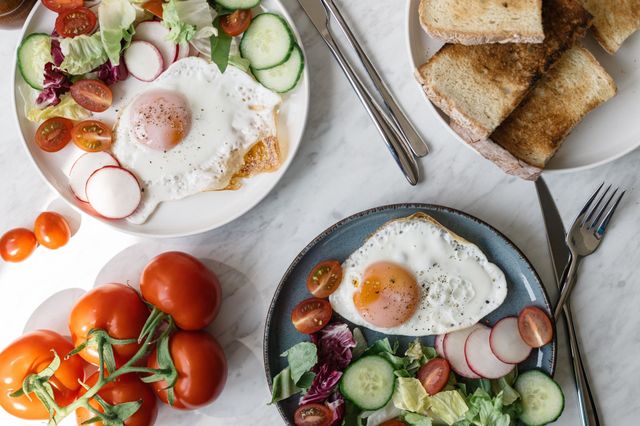 Brekfast food served at home, consisting of eggs, colorful salad, tomatoes, fresh baked bread.