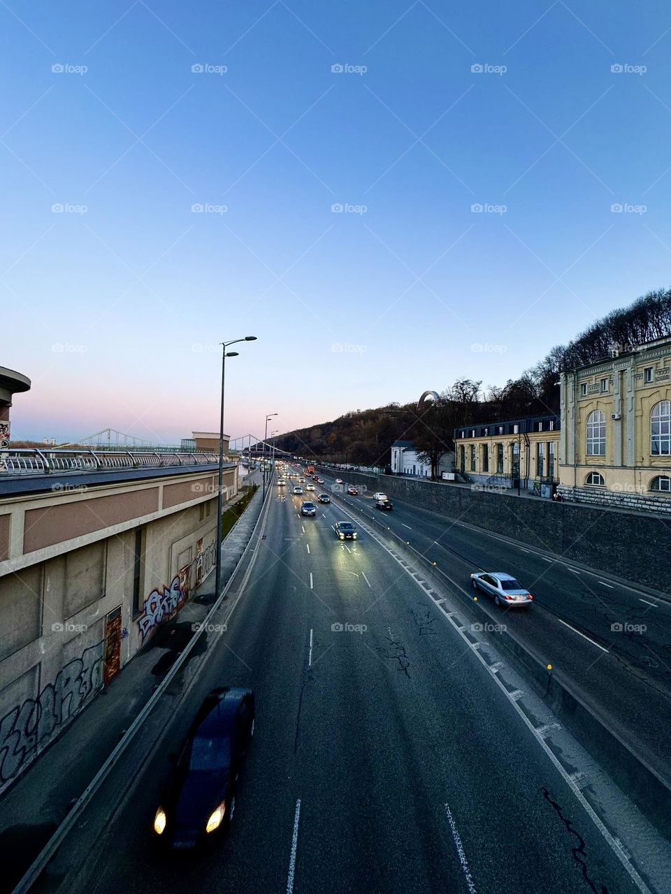 Вечерний закат окрашивает небо в оранжевые и розовые оттенки, освещая дорогу, по которой движутся машины. Мягкий свет создает умиротворение и тепло, приглашая в увлекательное путешествие 