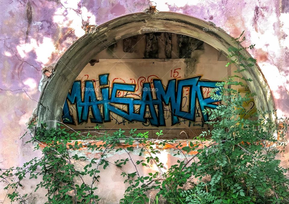 Through the unglazed window of an abandoned hotel the words “mais amor” (more love) can be seen graffitied on the wall
