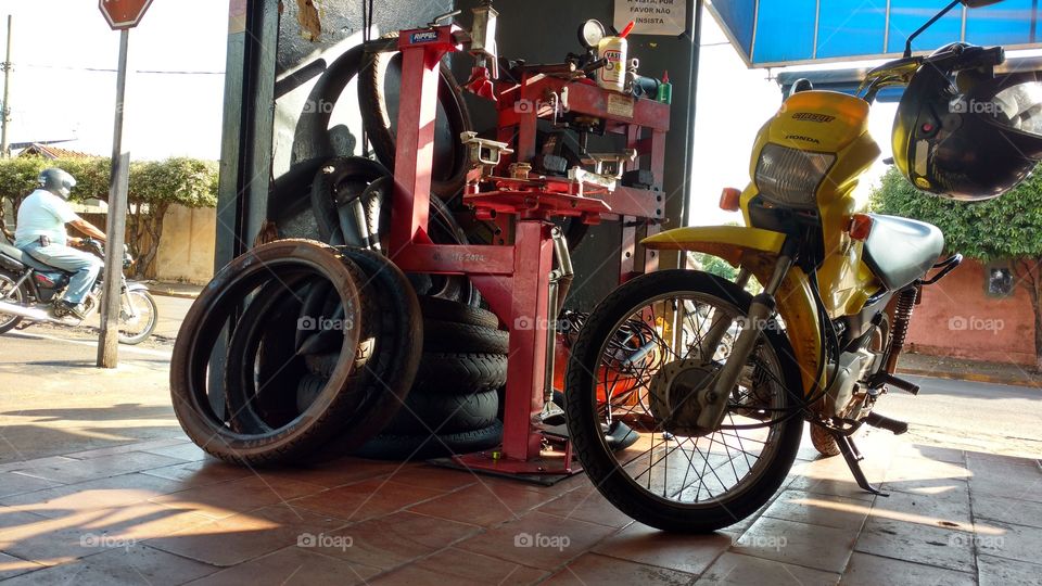 Dentro de oficina mecânica de motocicletas. Homem de moto na rua.