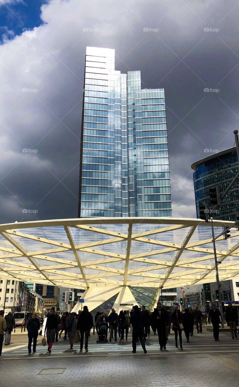 Office building tower against a dark stormy sky in the background and silhouettes of people in the foreground. 