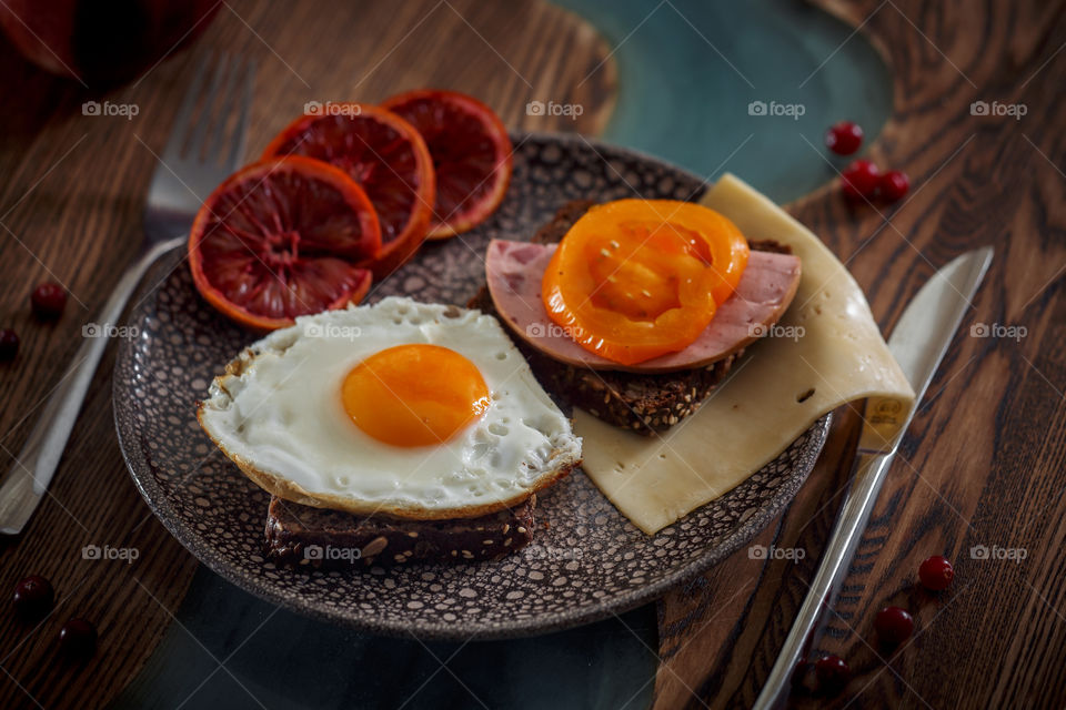 Grain bread with egg, tomato, cheese and bacon on ceramic plate with red orange to desert