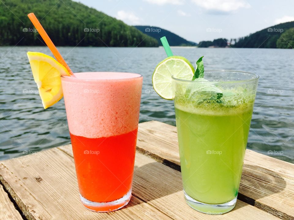 Strawberry lemonade and mint lemonade glasses near the lake