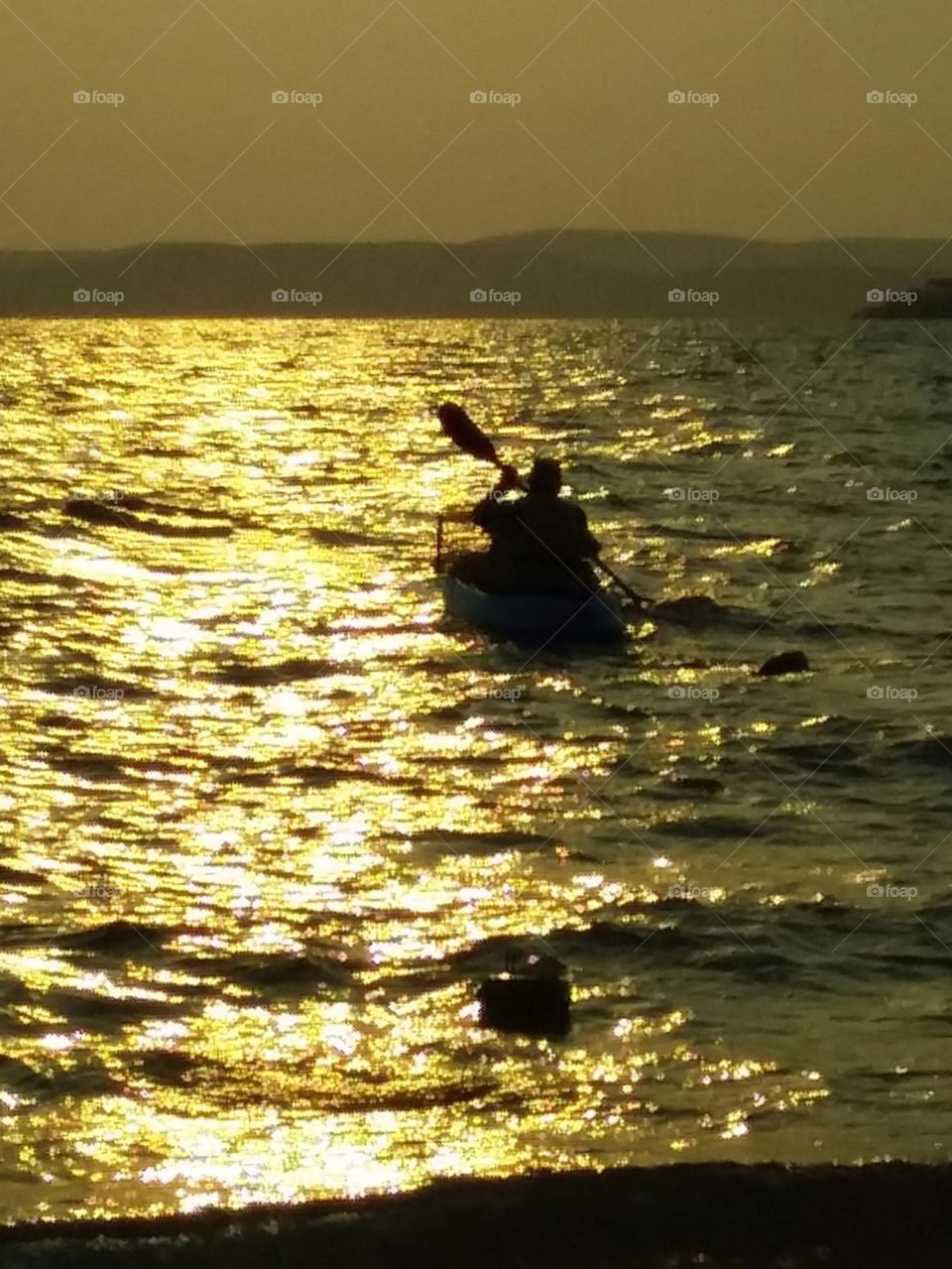 man in canoe silhouetted on golden sunrise water