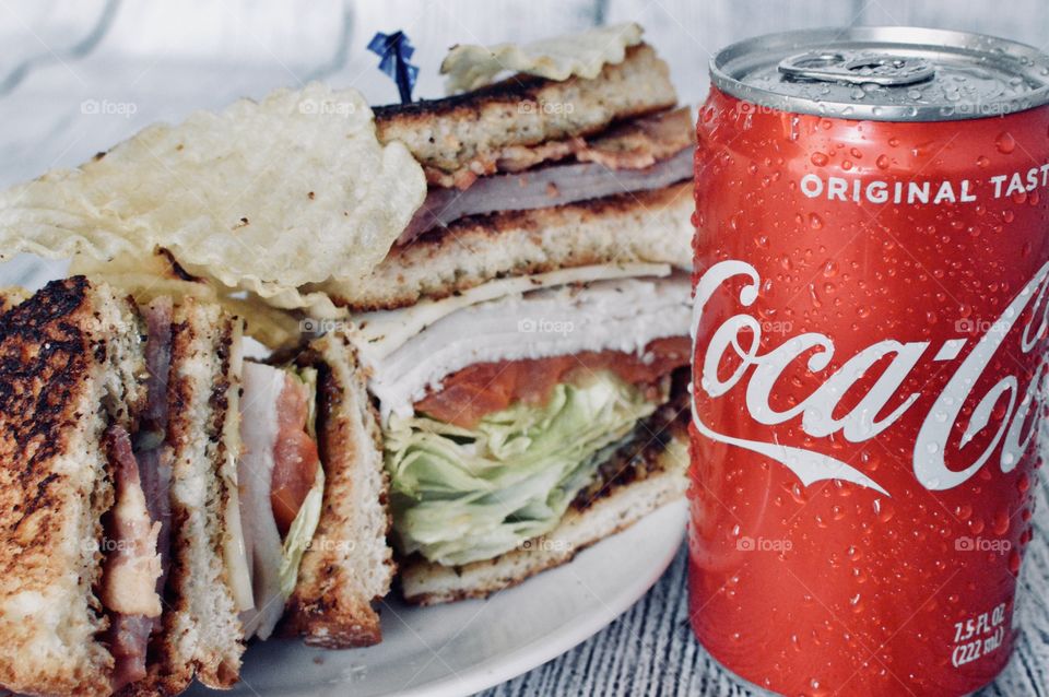 A can of Coca Cola with a club sandwich on a white rustic background 