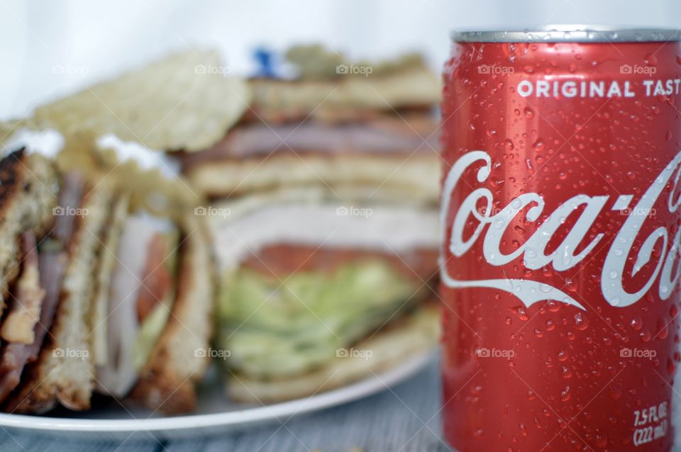 A can and a Bottle of Coca Cola with a club sandwich on a white rustic background 