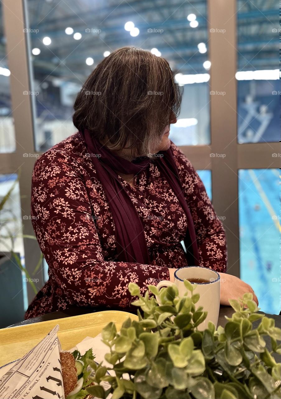 Woman watcing swimmers by the window at swimming hall cafe @ Mäkelänrinteen uintikeskus, Helsinki, Finland