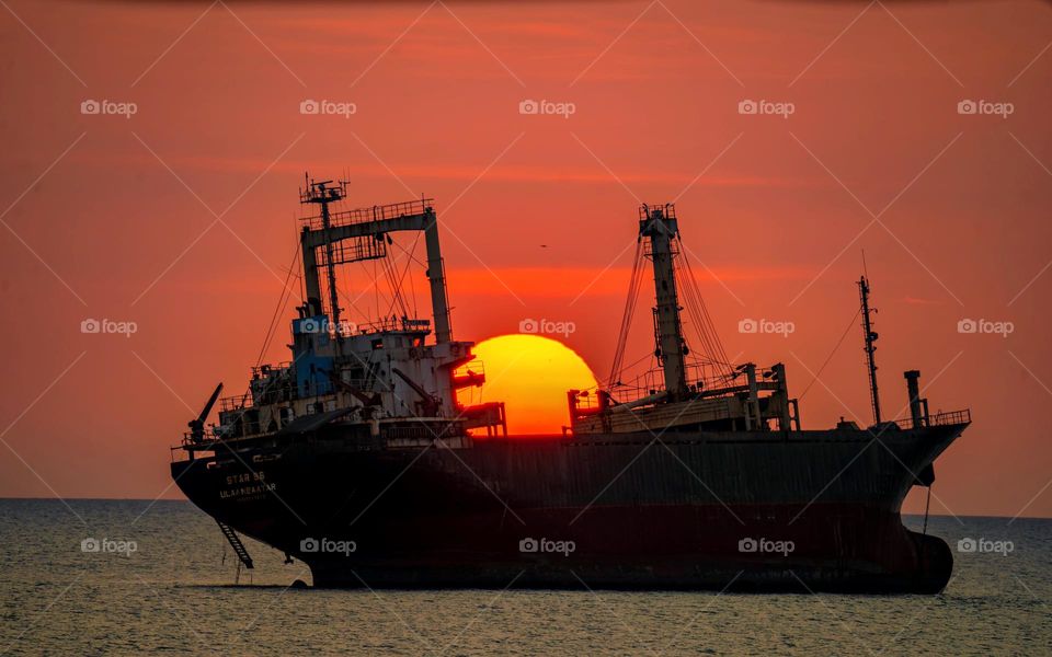 The magnificent Sunset Over the Vast Sea: A Majestic Ship Silhouetted Against the Radiant Red Sky