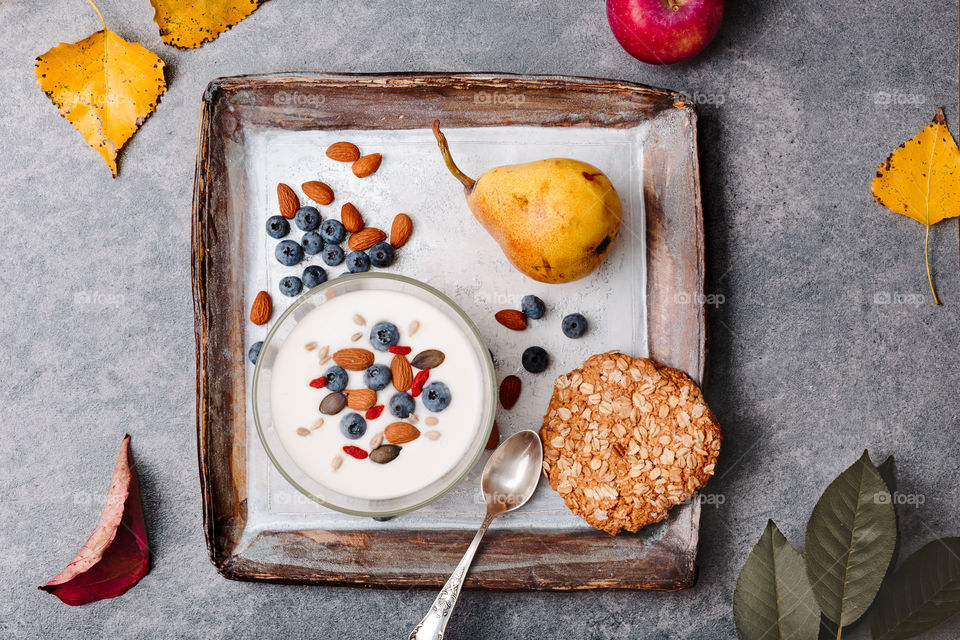 Breakfast on table. Yogurt with added blueberries and roasted almonds. Muesli cookie, apples and pears on table. Light and healthy meal. Good quality balanced diet. Flat top-down composition