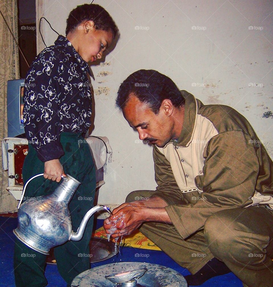Son assists his father with washing his hands before eating.
