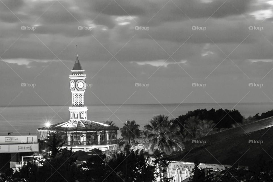 Black and white photo of clock tower and sea during the sunset