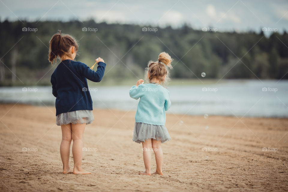 Little sisters on lake coast at sunny evening. 