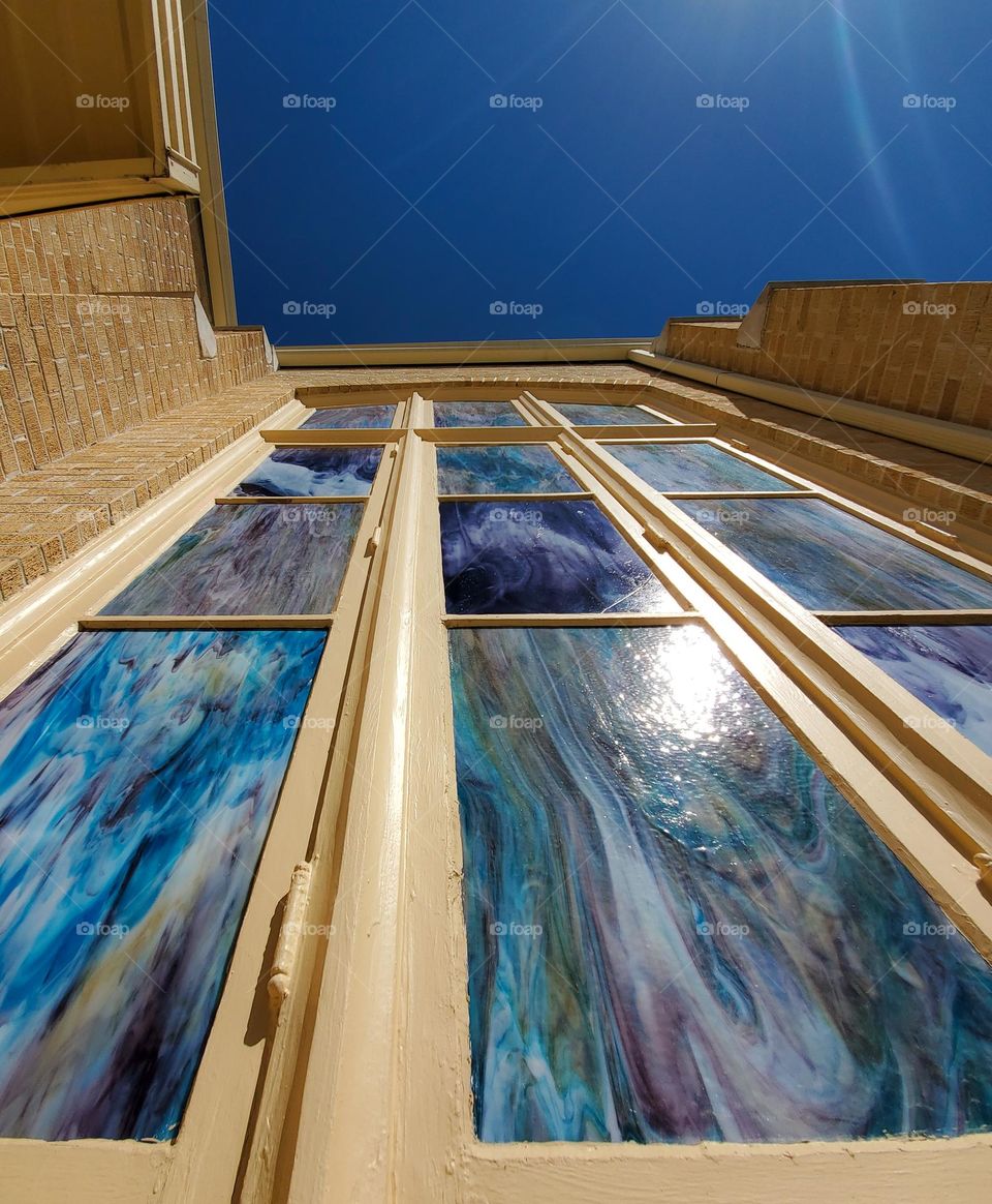 Looking up at second floor beautiful marble design stained glass window rectangles lites with hues of blue,  purple, and greens.