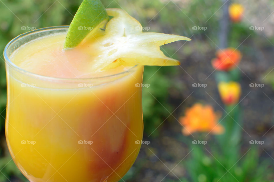 Fresh fruit smoothie mixed blended drink with white and pink smoothie infused together  in garden with flowers in background and lime star fruit garnish 