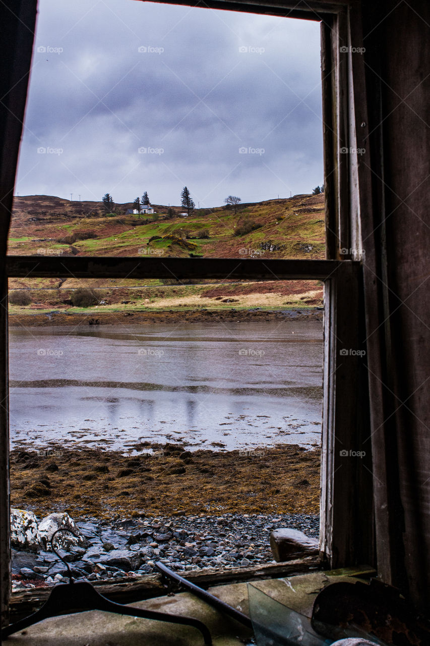 View from an abandoned and derelict cottage window out onto the loch, hills and moody sky. Isle of Skye, Scotland 