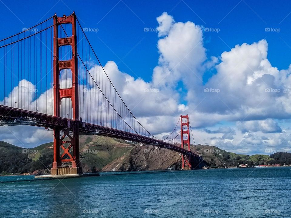 Stunning view of the Golden Gate Bridge in San Francisco California with fluffy white clouds against a beautiful blue sky with calm waters of the Pacific Ocean 