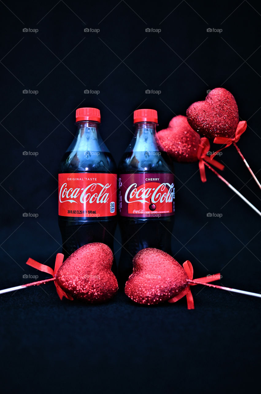 Close up shot of two Coca Cola with black background with the mists at the studio with hearts. 