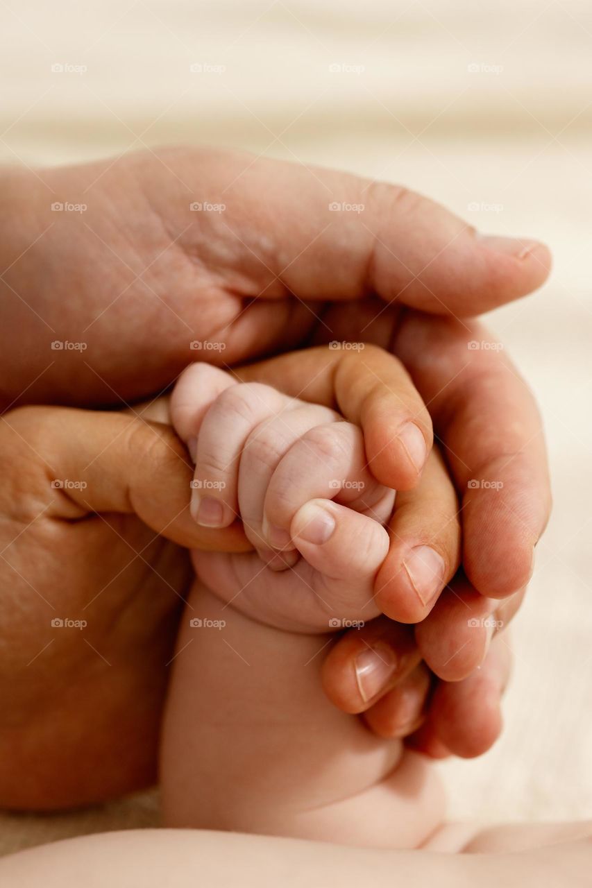 The baby's hand is in the hands of dad and mom.