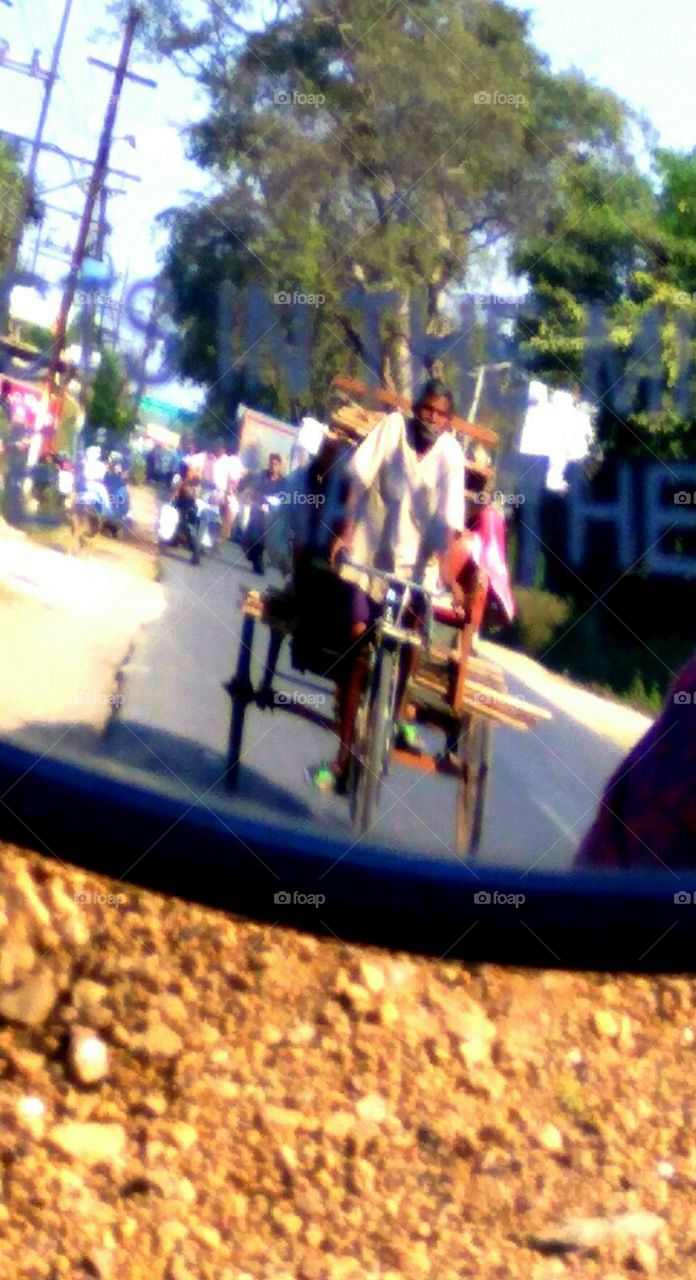 A snapshot of a rickshaw puller through rear mirror of bike...