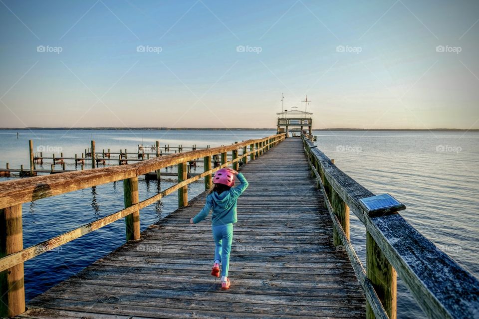 A little girl dash along a peer still wearing her bicycle helmet, exited to join her friend to watch the sunset. 