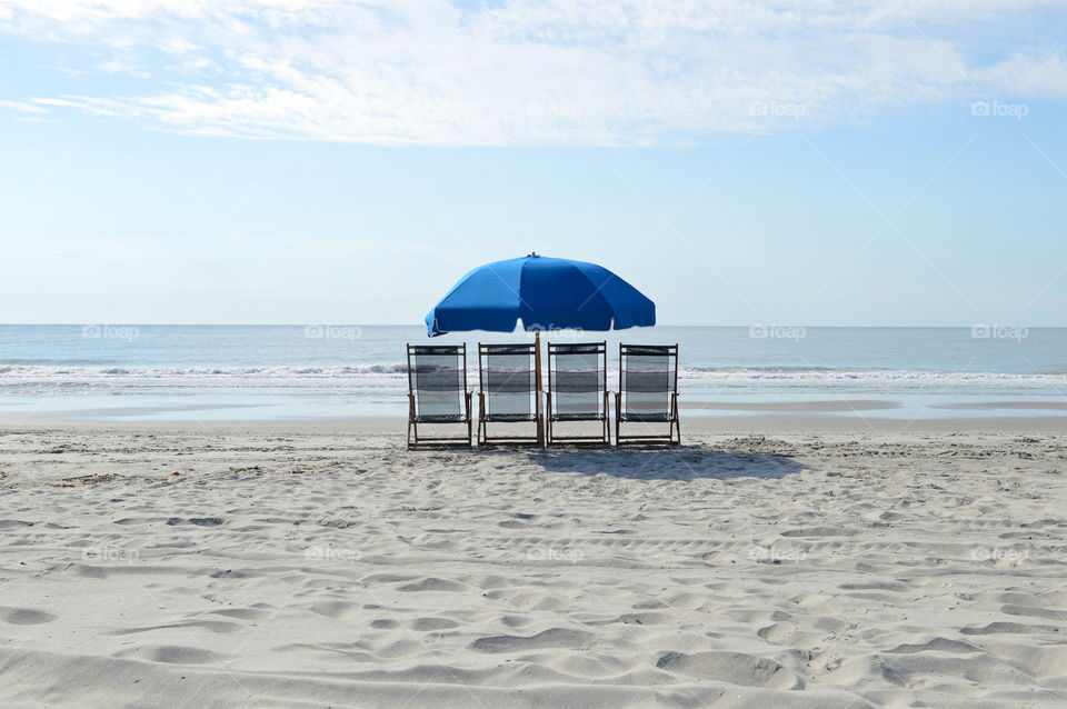 Group of lounge chairs lined up with an umbrella on the beach shore overlooking the ocean