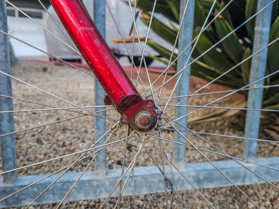  Abstract Vintage red bicycle along a fence highlighting the front wheel spokes 