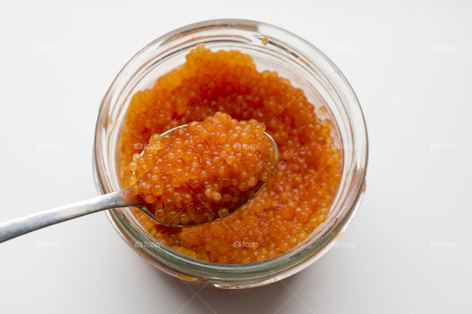 Orange caviar on a spoon above a glass jar 