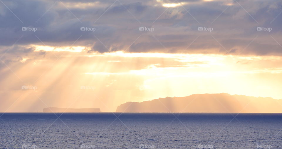 sun beams between gray clouds in the sky over deserted Madeira Islands and Atlantic Ocean in early morning