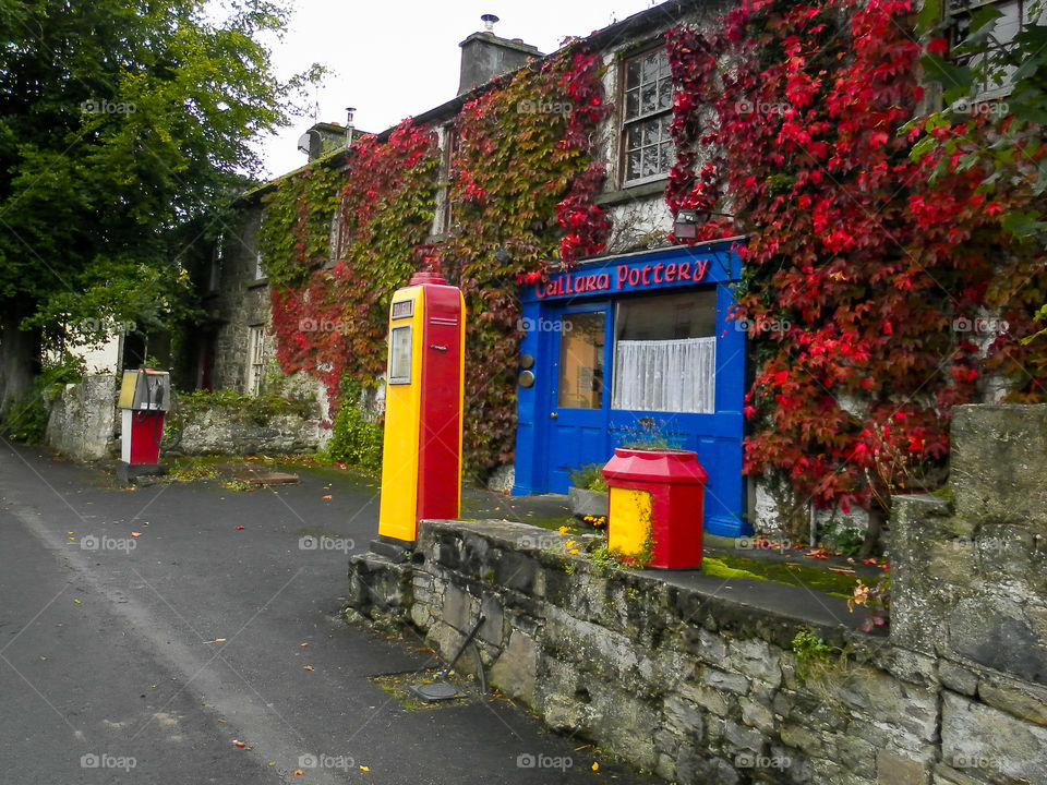 The color red is the main focus of this composition. Image of building with red ivy and old red and yellow petrol station