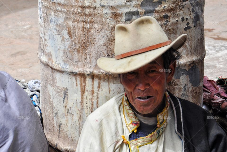 old man in the hat sitting in the yard of buddhist monastery in tibet