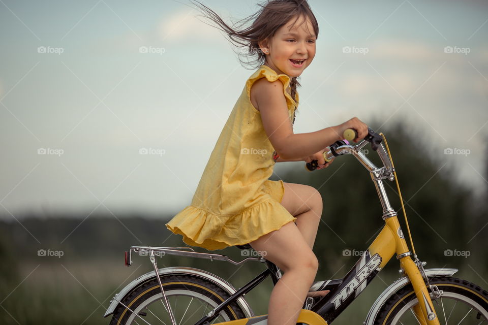 Little girl with bicycle in the summer field 