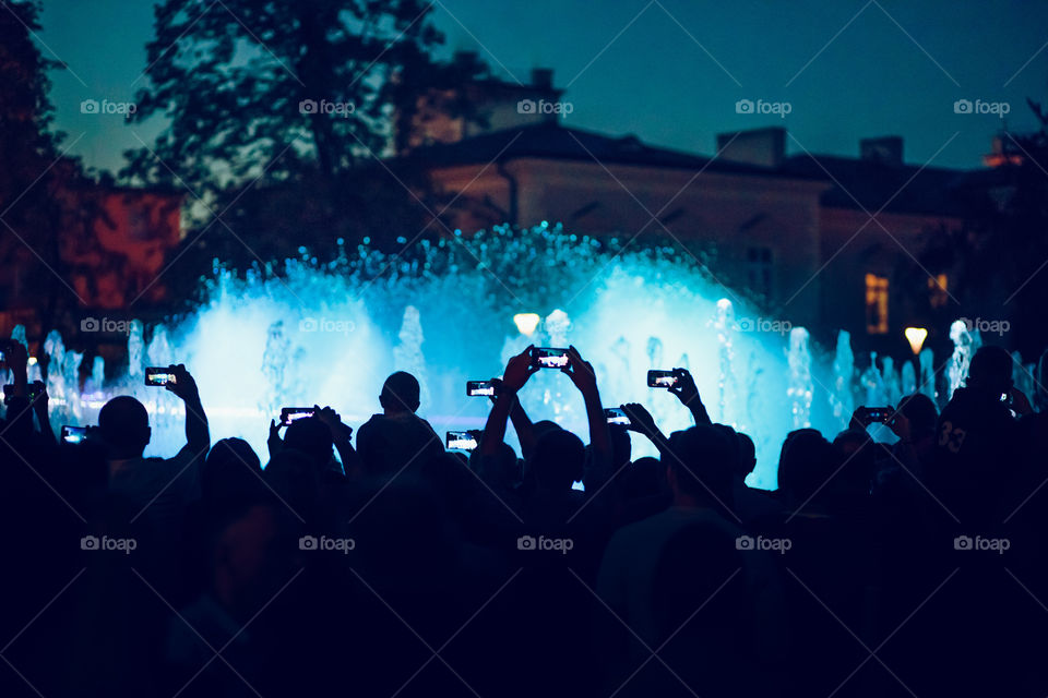 People taking photos of fountain and lights with smartphones in the evening in the center of Lublin