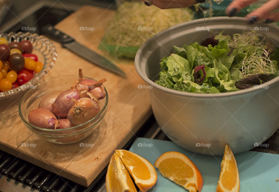 Making a healthy salad with mixed lettuce, spinach, orange, French shallots, tomato and sprouts 