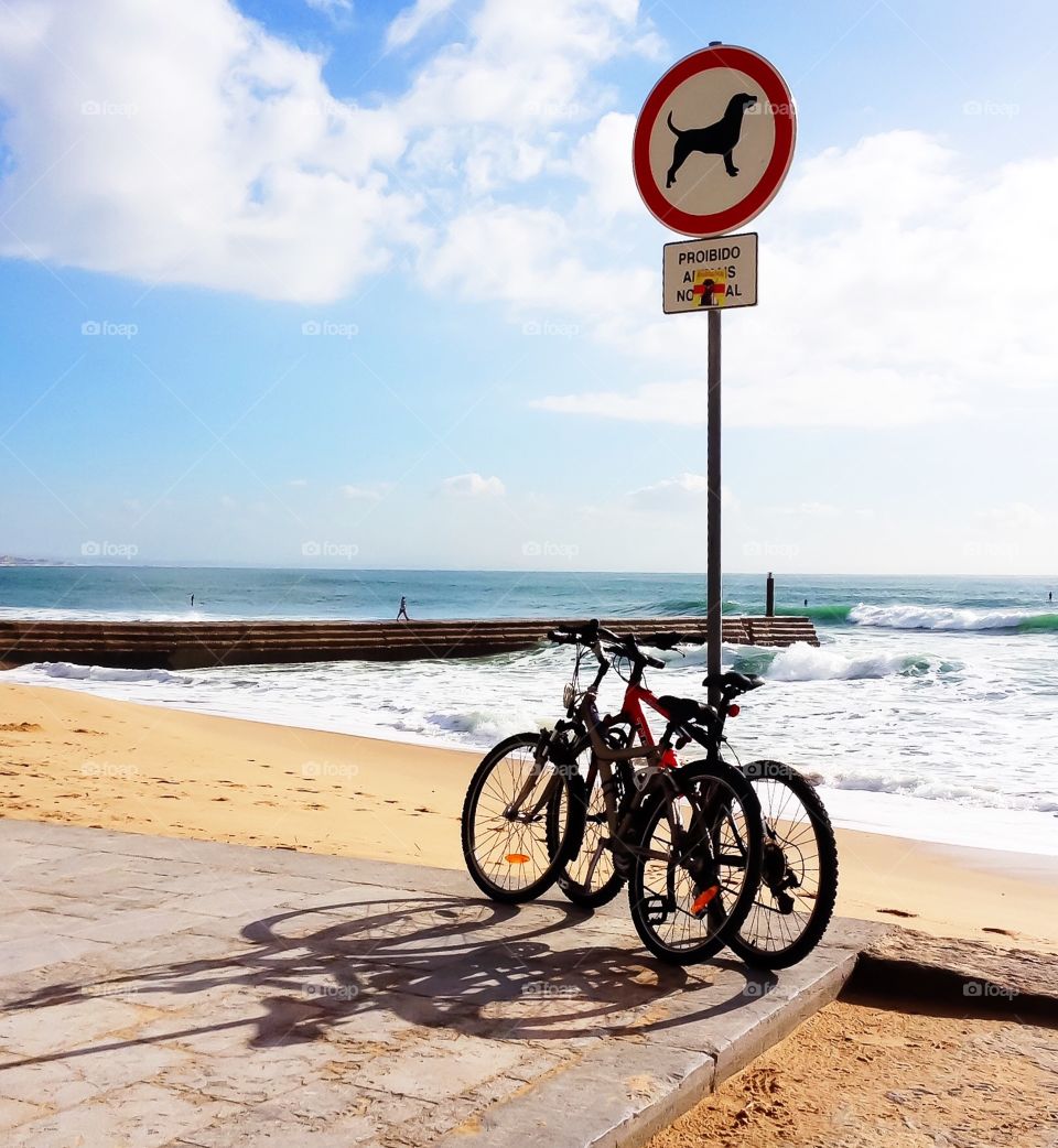 Two bikes on the waterfront near sign. Stone pier goes onto the ocean