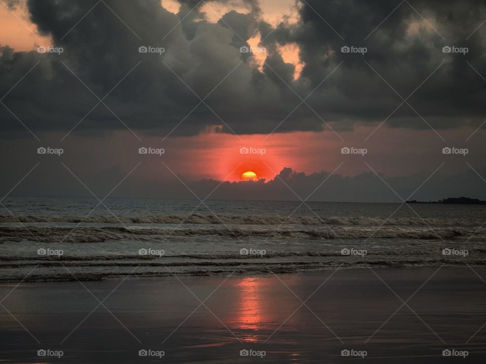 Awesome ending of sunset on the beach in a cloudy day and calm waves on the ocean.