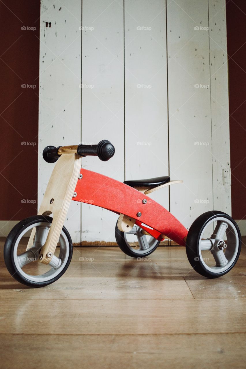A modern composition of a childen tricycle in front of an old wooden door
