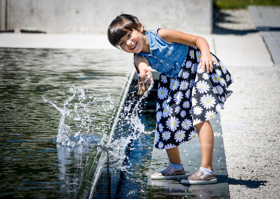 Cute girl is playing with water in a fontain in summer