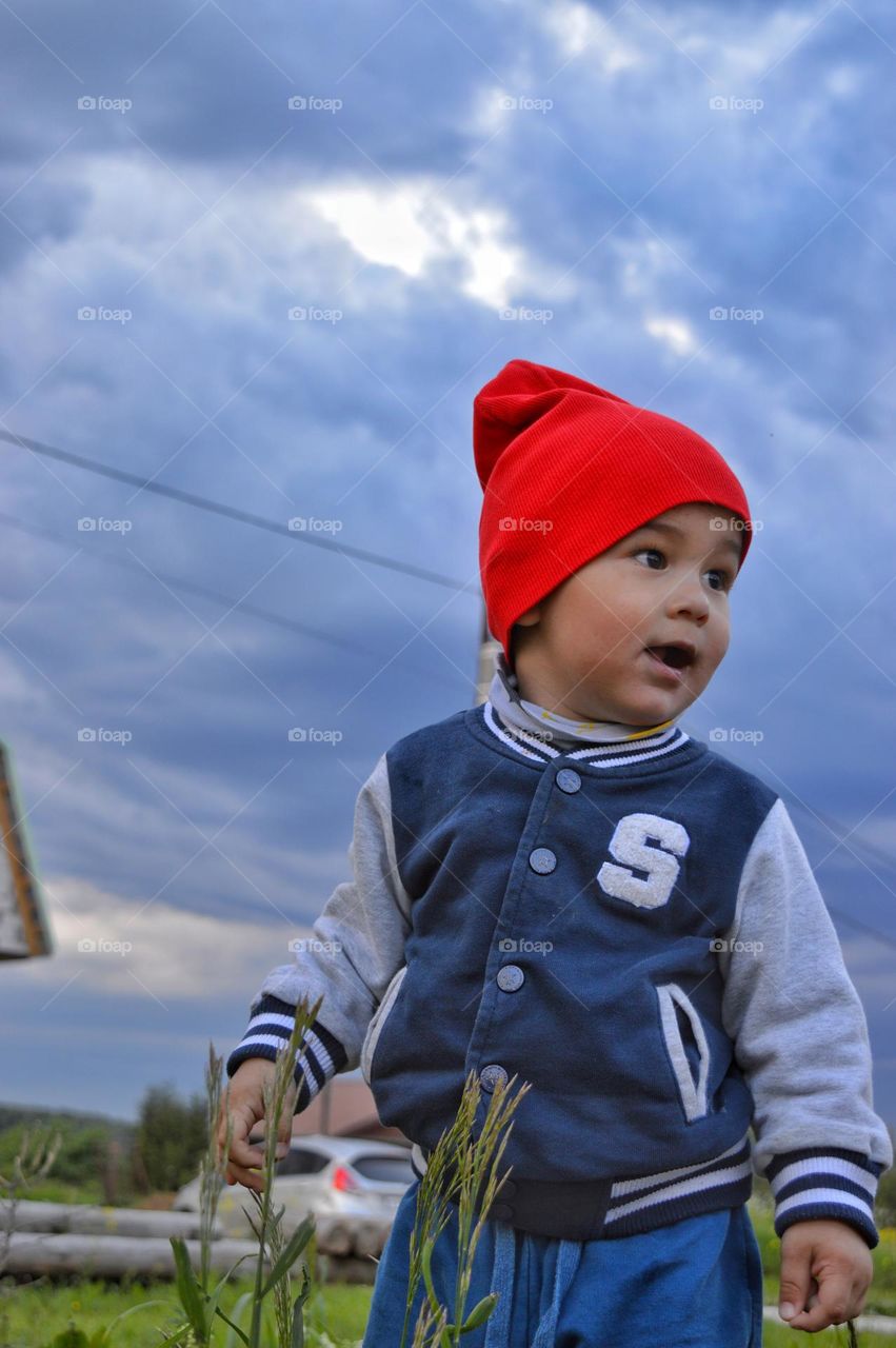 a boy in a red hat looks around admiringly. gray-blue clouds in the background.