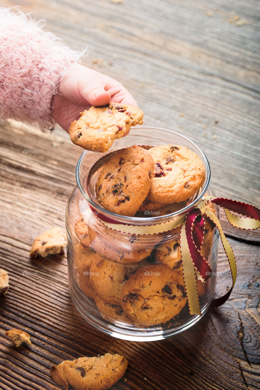 Little girl taking a cookie from a jar filled with oat cookies standing on a wooden table