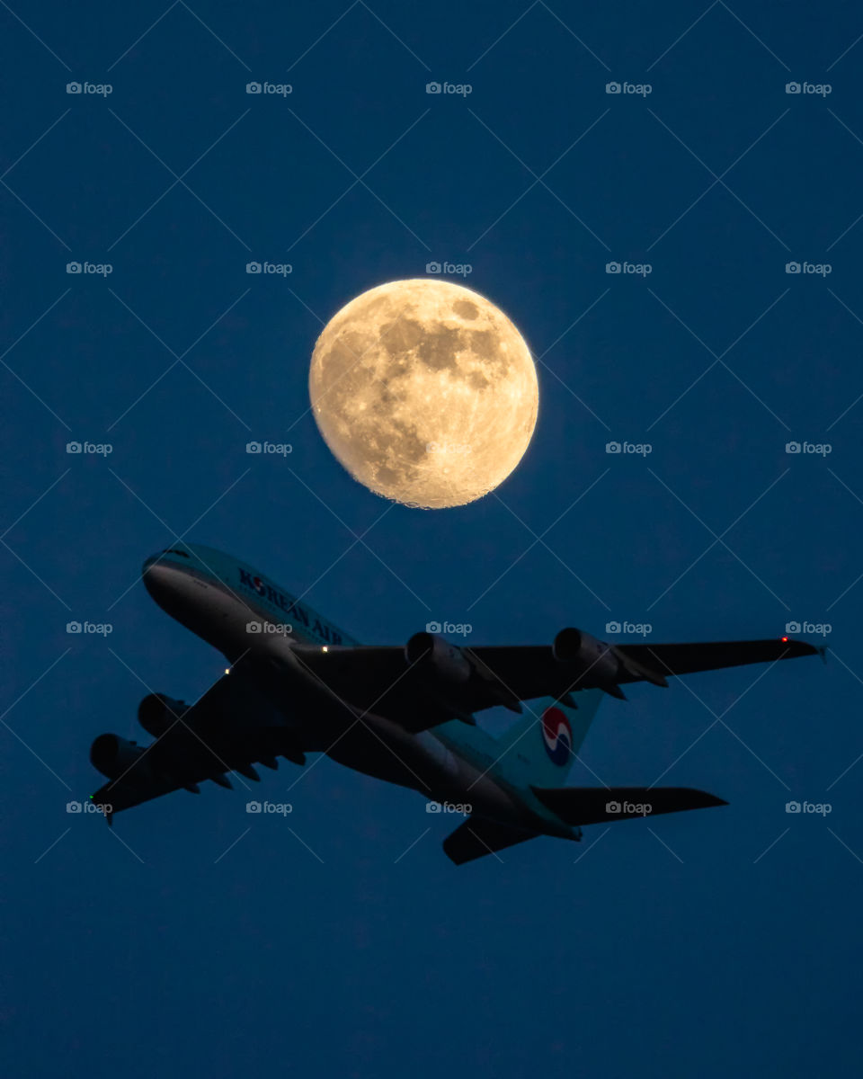 A huge A380 airbus flying through the evening sky past an almost full moon. 