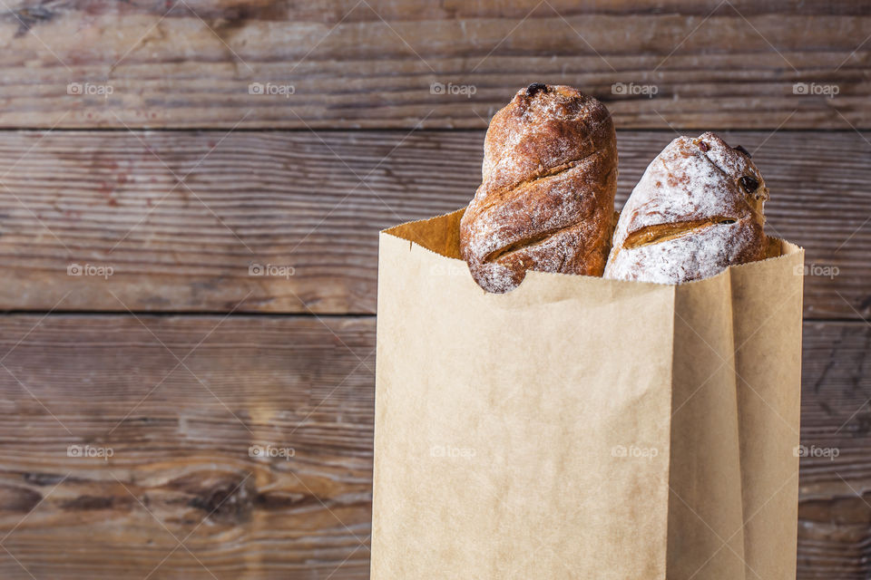 Paper bag with two breads on wooden table