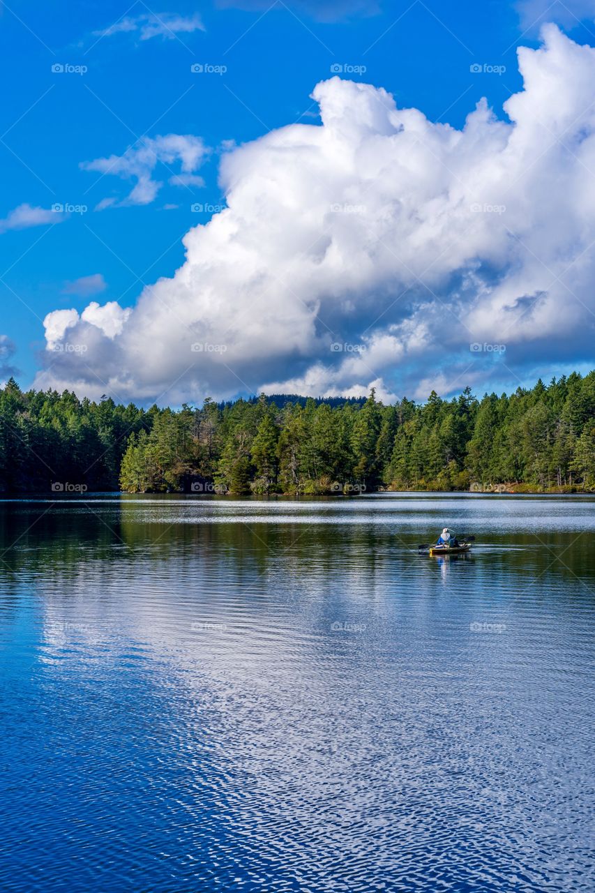 Man in yellow boat fishing on a scenic reflective lake 
