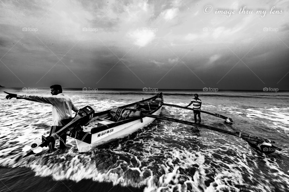 fishermen pulling a fishing boat out of sea in monsoon