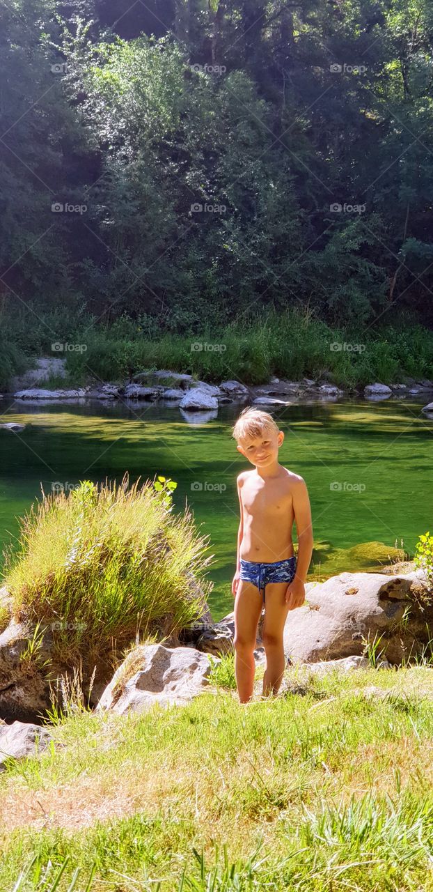 a boy standing by the shore of a mountain river