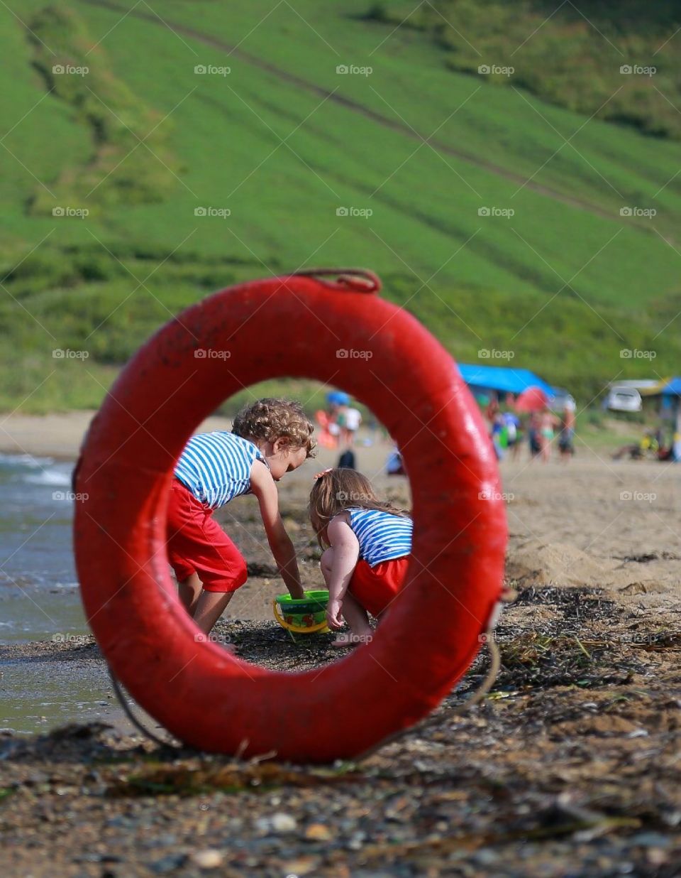 boy and girl on the beach in striped nautical shirts and red shorts play on the sand by the sea, they can be seen through a red lifebuoy, childhood, children play, sea, vacation, red