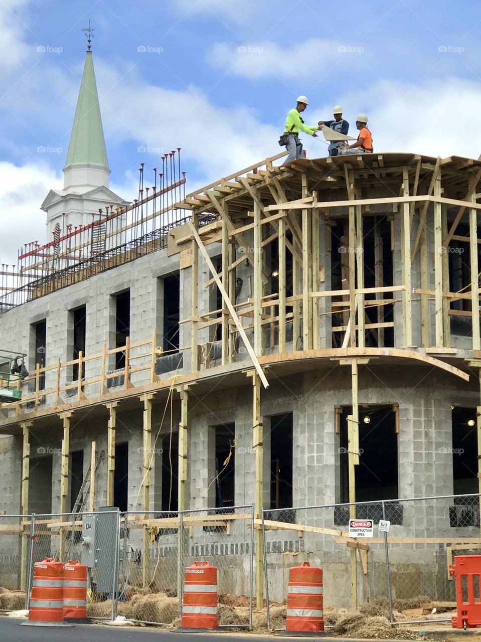 Construction men at work on a new two story building with a contrasting historic steeple in the background 